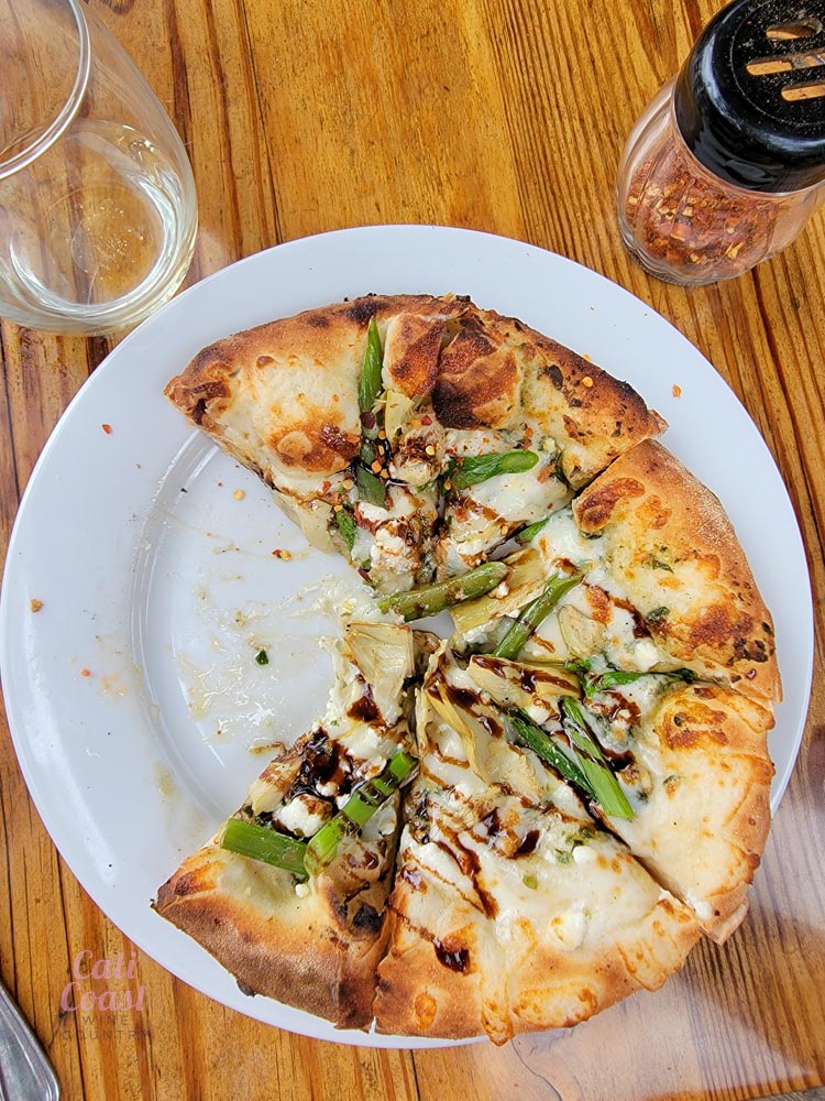 Half-eaten asparagus artisan pizza on wooden table.