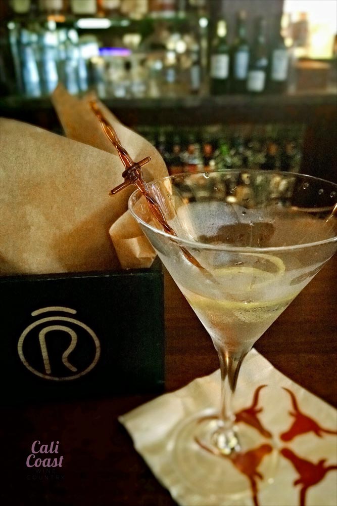 Martini with lemon peel at a bar counter.