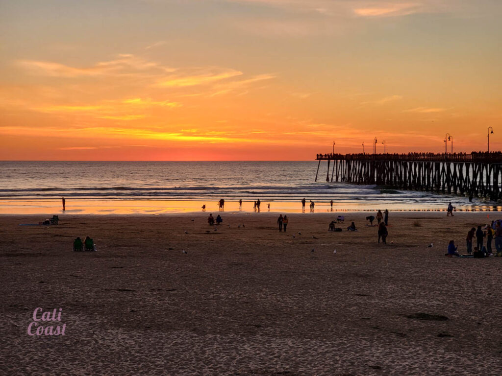 Sunset over beach and ocean pier, people watching.