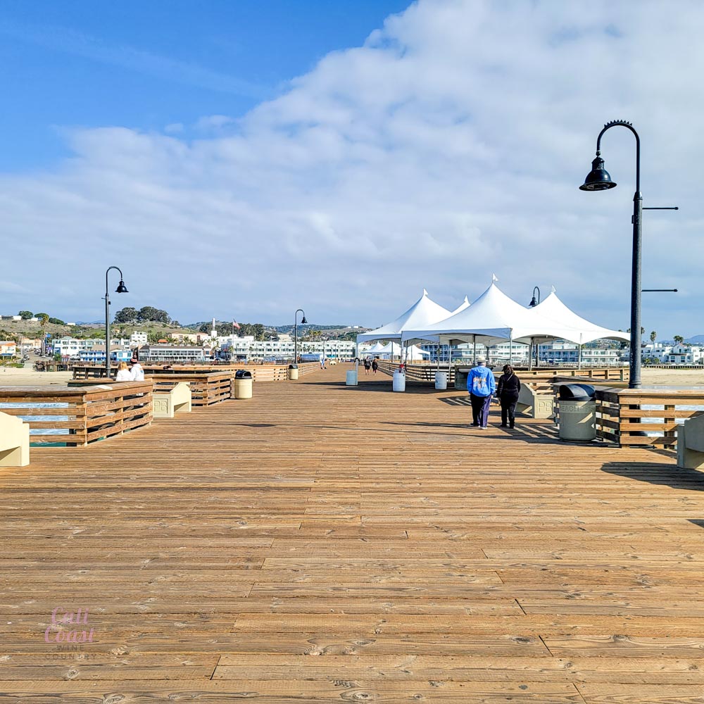 Sunny pier with tents and people walking.